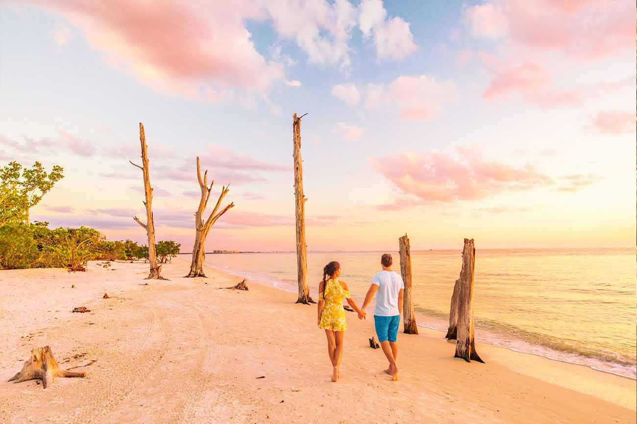 Couple walking on beach at sunset romantic travel getaway, idyllic Florida destination, Lovers key beach state park in the gulf of Mexico. Woman and man holding hands relaxing. Southwest Florida.