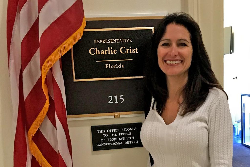 Leslie standing in front of placard and American flag.