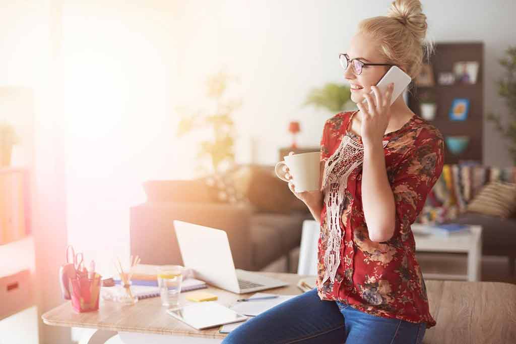 Woman holding phone talking on it with a cup of coffee in other hand