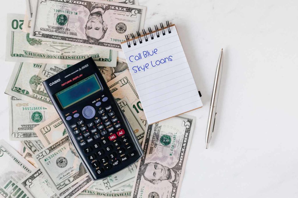 Calculator sitting atop of money next to a notepad and pen