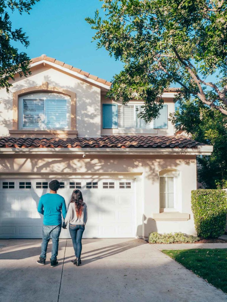 couple standing in driveway looking at new home