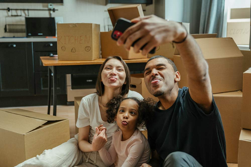 couple and child taking selfie near moving boxes