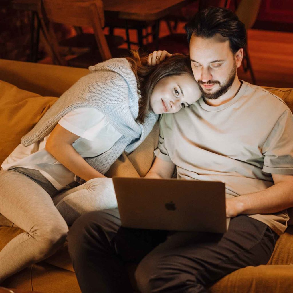 Couple lounging on sofa looking at laptop screen