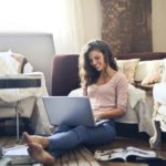 Woman sitting on floor smiling while using laptop