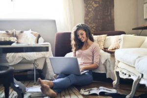 Woman sitting on floor smiling while using laptop