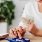 person using calculator holding pen and cash