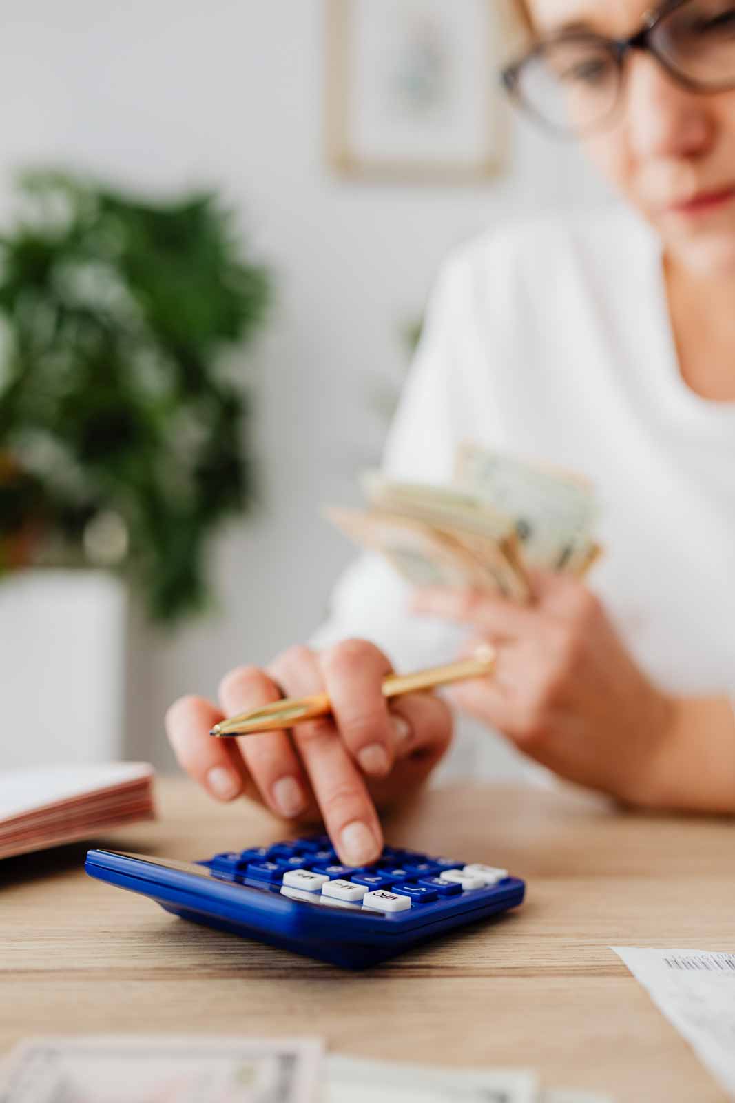 person using calculator holding pen and cash