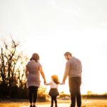 A couple holding hands with a young child walking toward the sunset.
