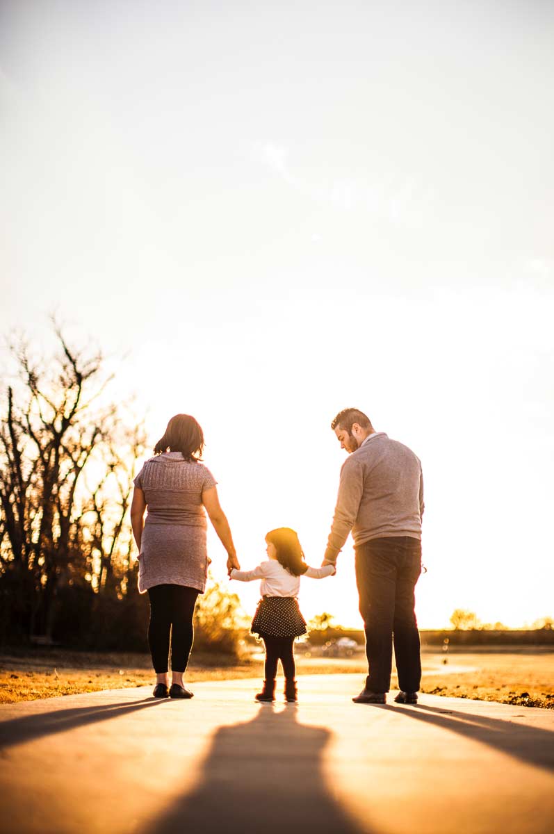 A couple holding hands with a young child walking toward the sunset.