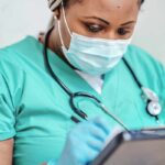 Nurse with mask writing on a clipboard.